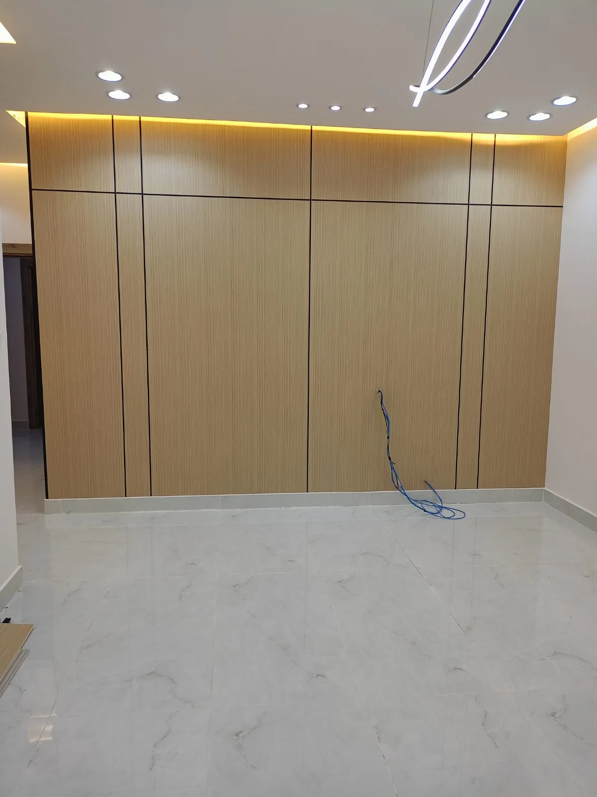 انواع بديل الشيبورد بالدمام بديل الشيبورد الدمام على جدار صالة مودرن، تتميز بخطوط تقسيم سوداء أنيقة وإضاءة LED مخفية في السقف