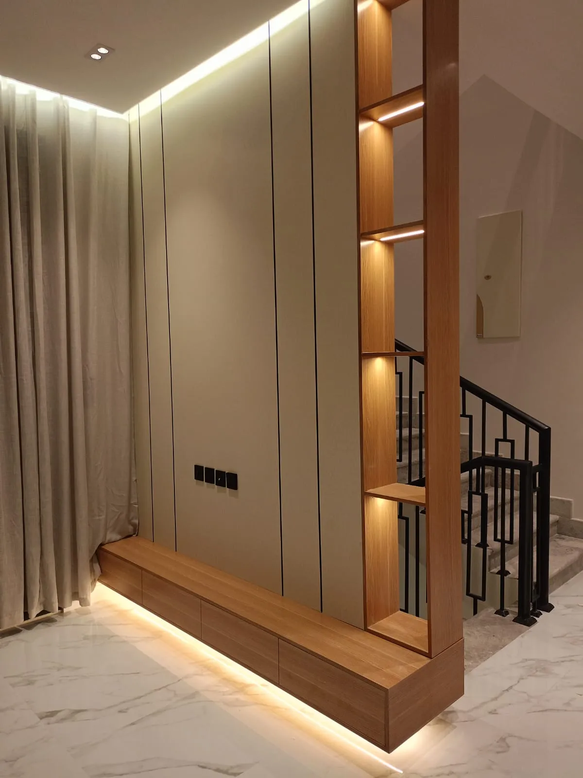 بديل الشيبورد باللون الكريمي يتميز بخطوط سوداء طولية وأرفف جانبية مضيئة، يفصل بين غرفة الجلوس والدرج