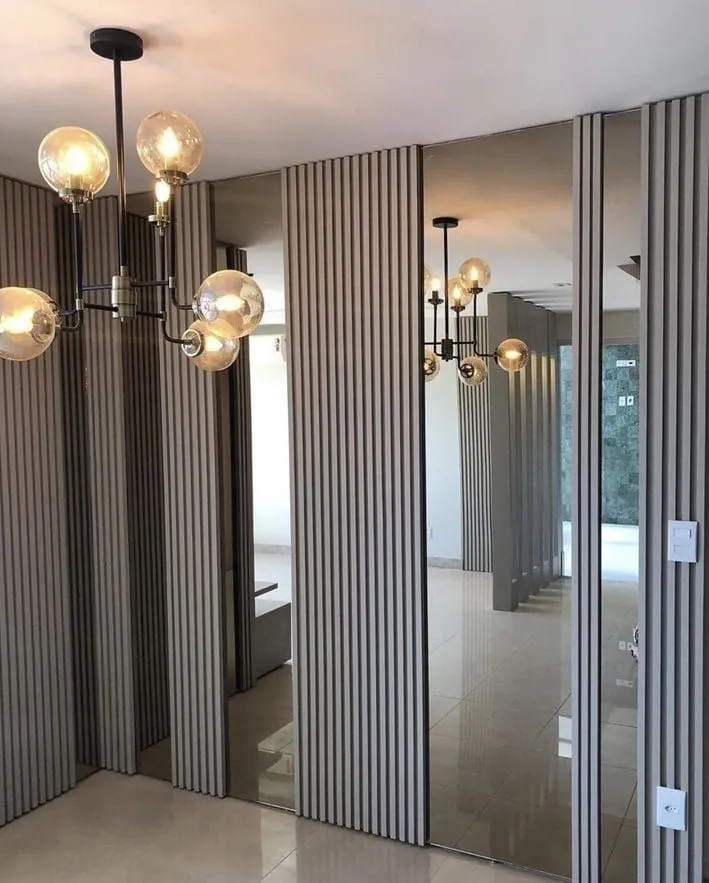 جدار داخلي يجمع بين ألواح بديل الخشب المضلعة والمرايا العاكسة مع إضاءة ثريا عصرية