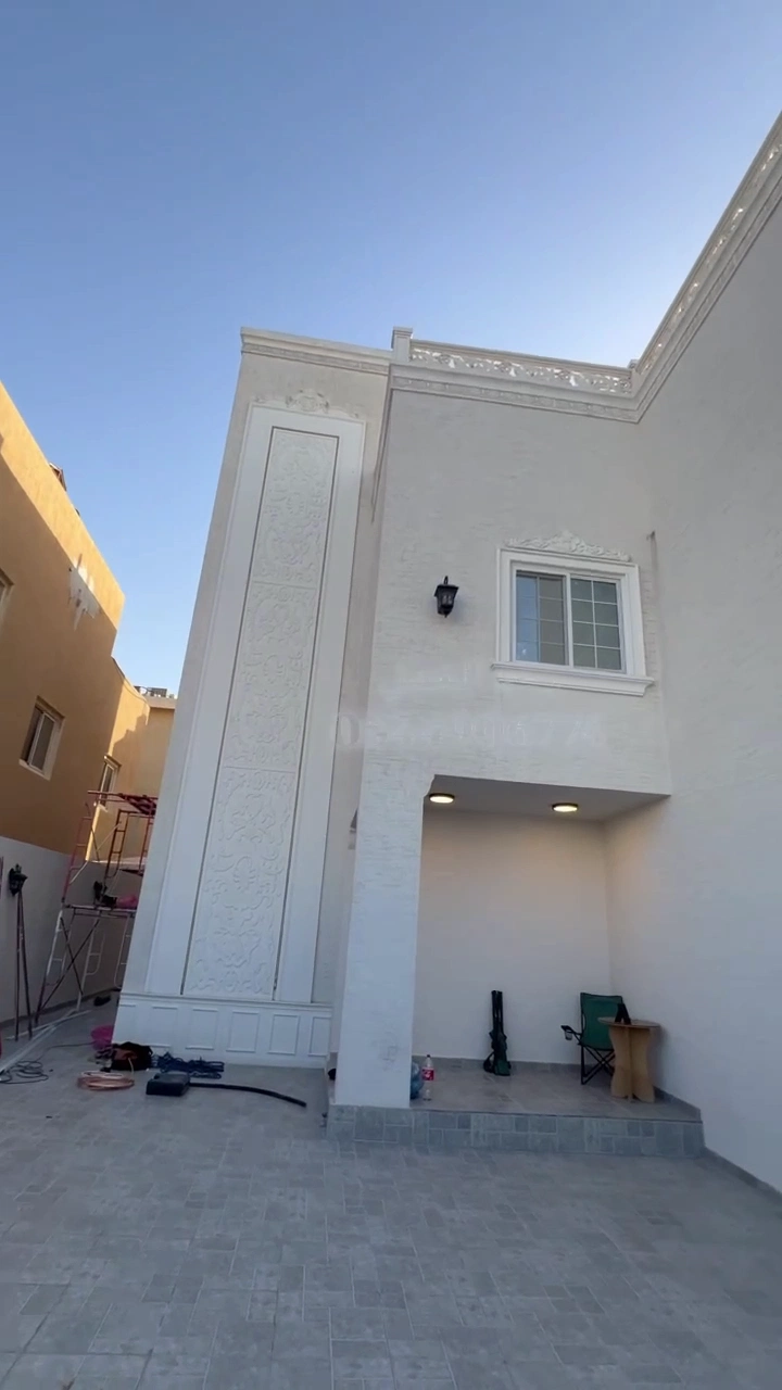 ديكورات الدمام : واجهة منزل بلون أبيض مزين بنقوش وزخارف فوم ، مع تفاصيل هندسية وإضاءة خارجية في مدخل الفناء