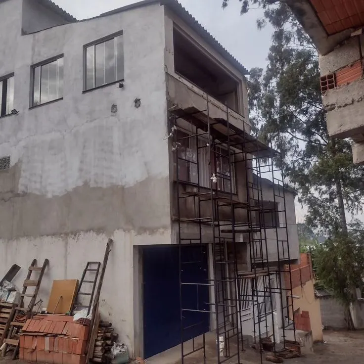 أعمال ترميم الواجهة الخارجية لمبنى سكني باستخدام السقالات المعدنية (الشدادات)، وهي خدمة يقدمها أفضل مقاول ترميم الدمام، تظهر مواد بناء كالطوب والسلالم في موقع العمل