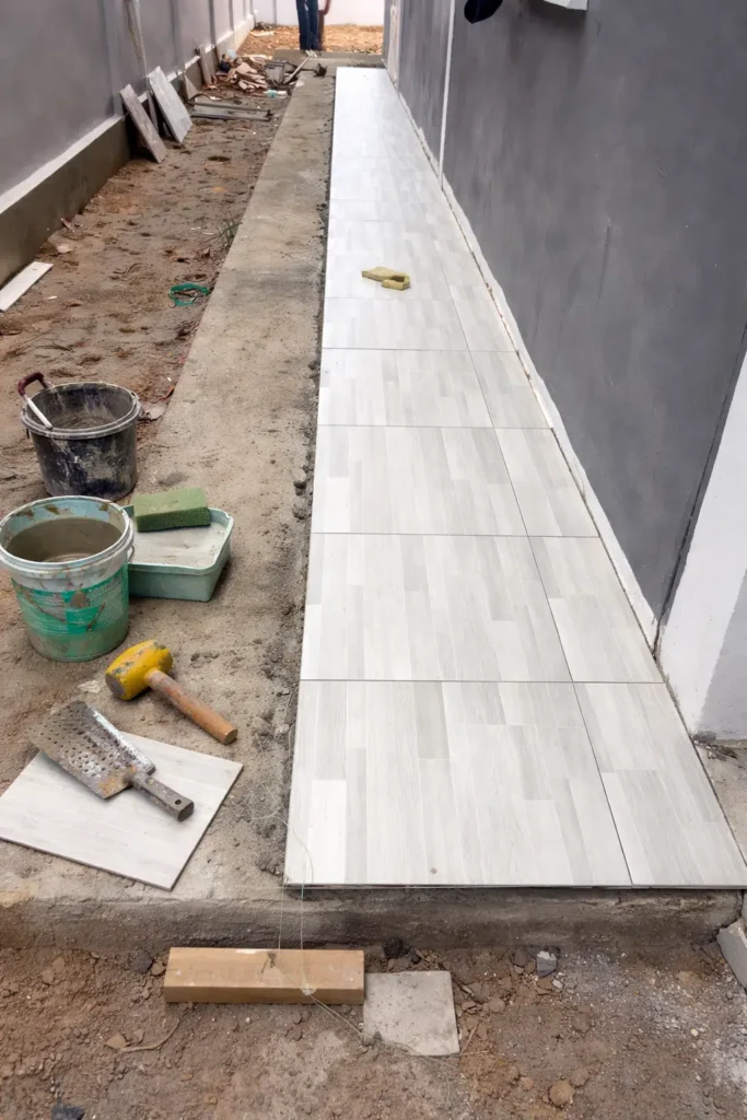 ممر خارجي بجانب جدار أثناء تنفيذ أعمال الترميم وتركيب بلاط أرضيات سيراميك مع ظهور أدوات التبليط ومواد البناء