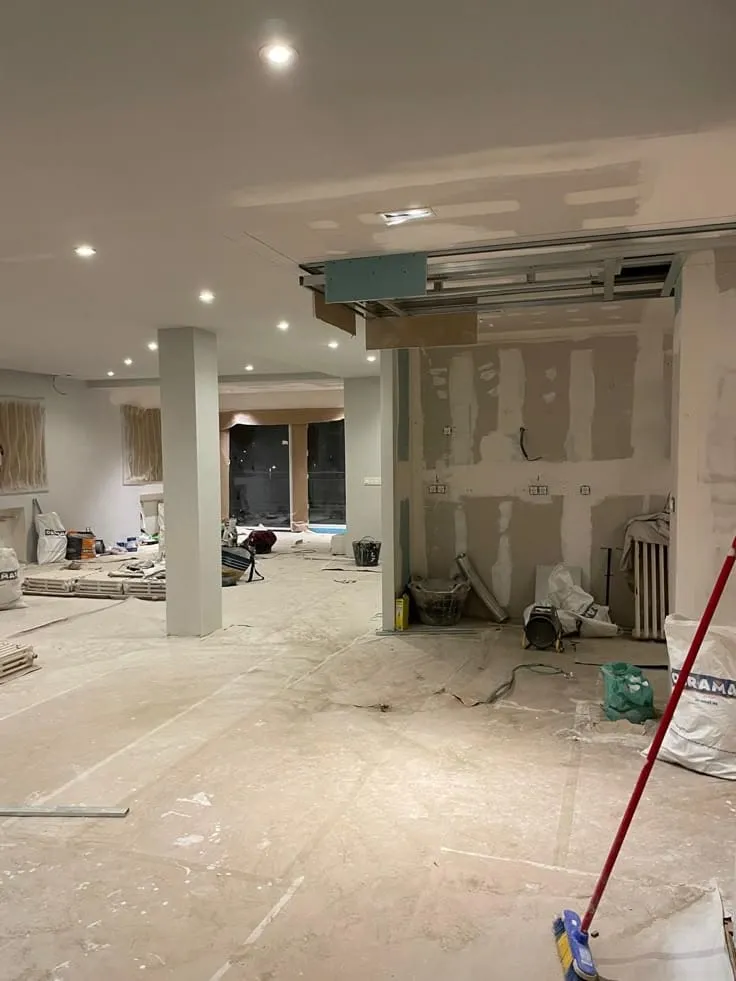 مقاول ترميم الدمام: مشروع ترميم وتشطيب داخلي قيد التنفيذ. تظهر الصورة مساحة واسعة مع جبس بورد أسقف شبه مكتملة وجدران جاهزة للتشطيب، مع وجود مواد بناء وأدوات عمل