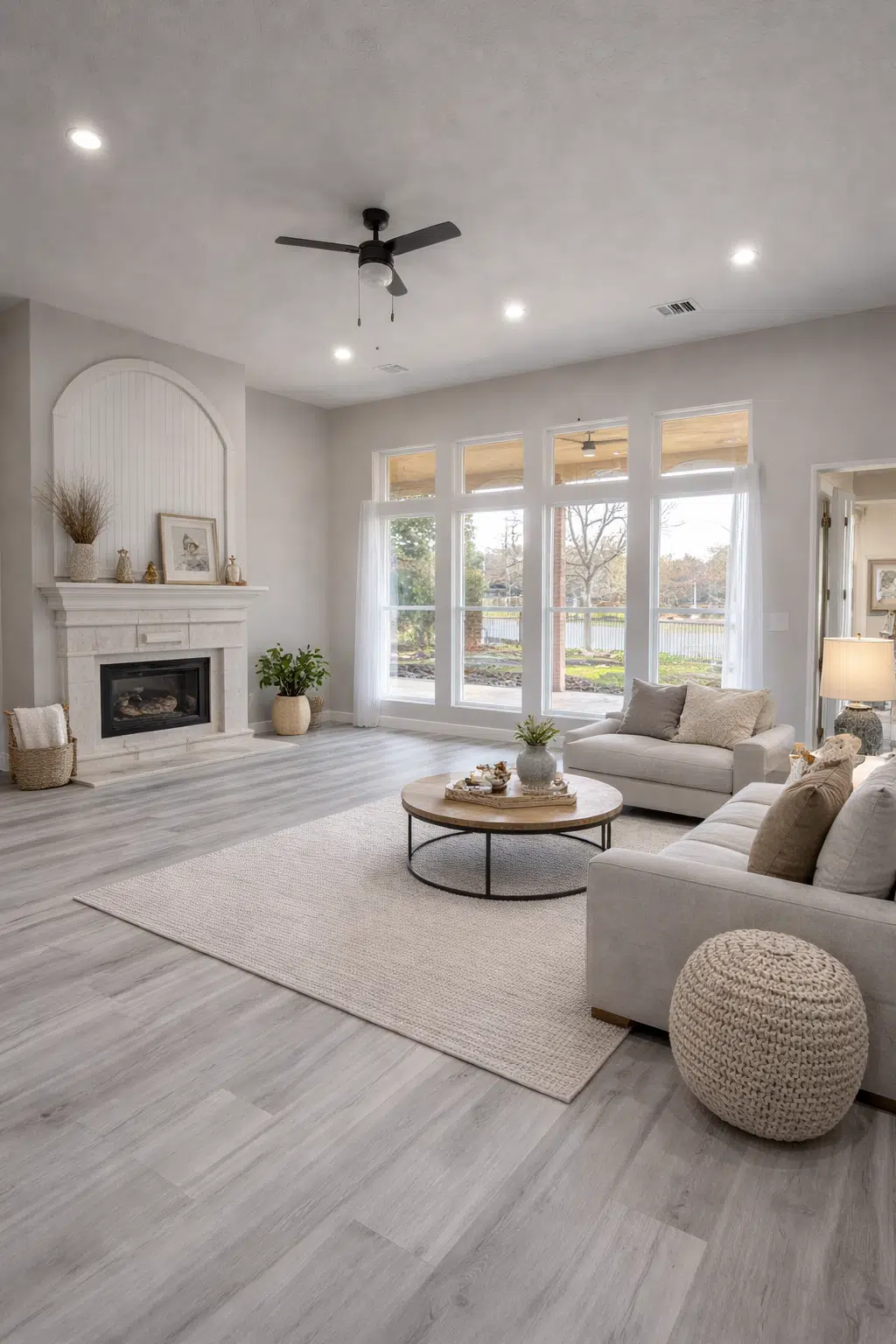 صالة تحتوي نوافذ زجاجية كبيرة وارضية باركيه مع مدفأة جدارية بيضاء وسقف بإنارة مخفية ومروحة عصرية