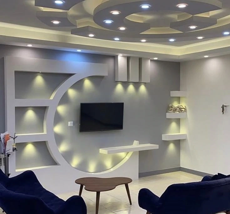 تصميم جبس بورد مودرن دائري لجدار التلفزيون مع أرفف داخلية وإضاءة صفراء وسقف دائري