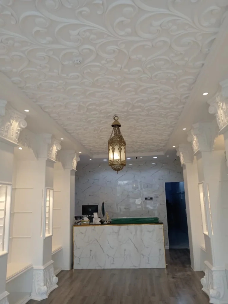 سقف جبس بورد مزخرف بنقوش بارزة باللون الأبيض، مع أعمدة جبسية مزخرفة وثريا نحاسية