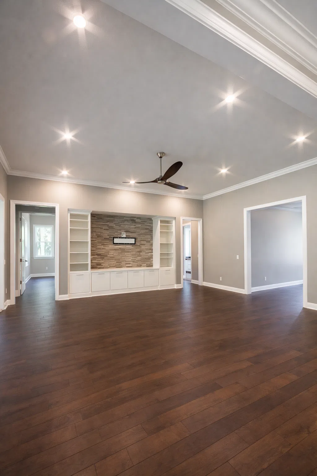 صالة كبيرة بتصميم حديث تحتوي على أرضية باركيه خشب لامع وسقف بإضاءة سبوت لايت ومروحة سقف عصرية