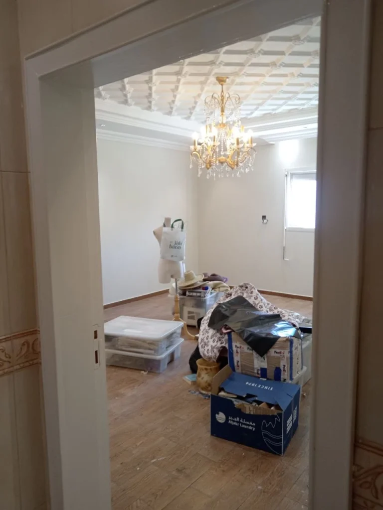 غرفة داخلية بتشطيب فاخر وسقف جبس مزخرف مع ثريا كلاسيكية وأرضية خشبية قبل ترتيب الأثاث