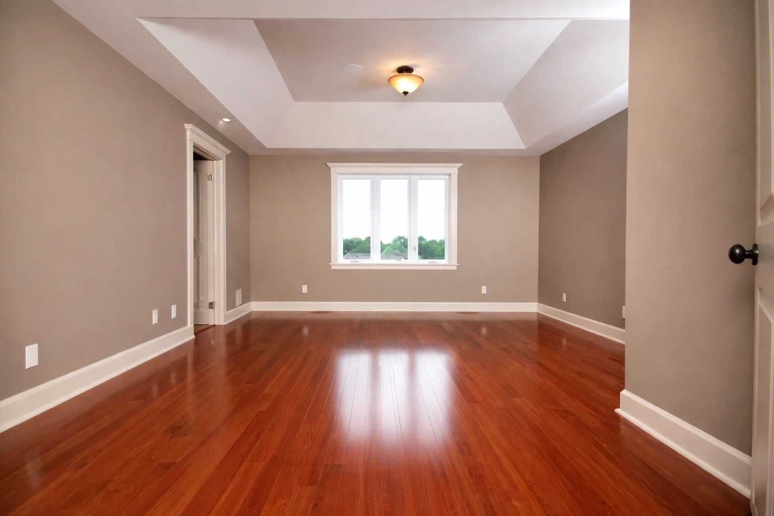 غرفة فارغة بتصميم عصري تحتوي على أرضية باركيه خشب بني لامع وسقف جبس بورد مع نافذة كبيرة