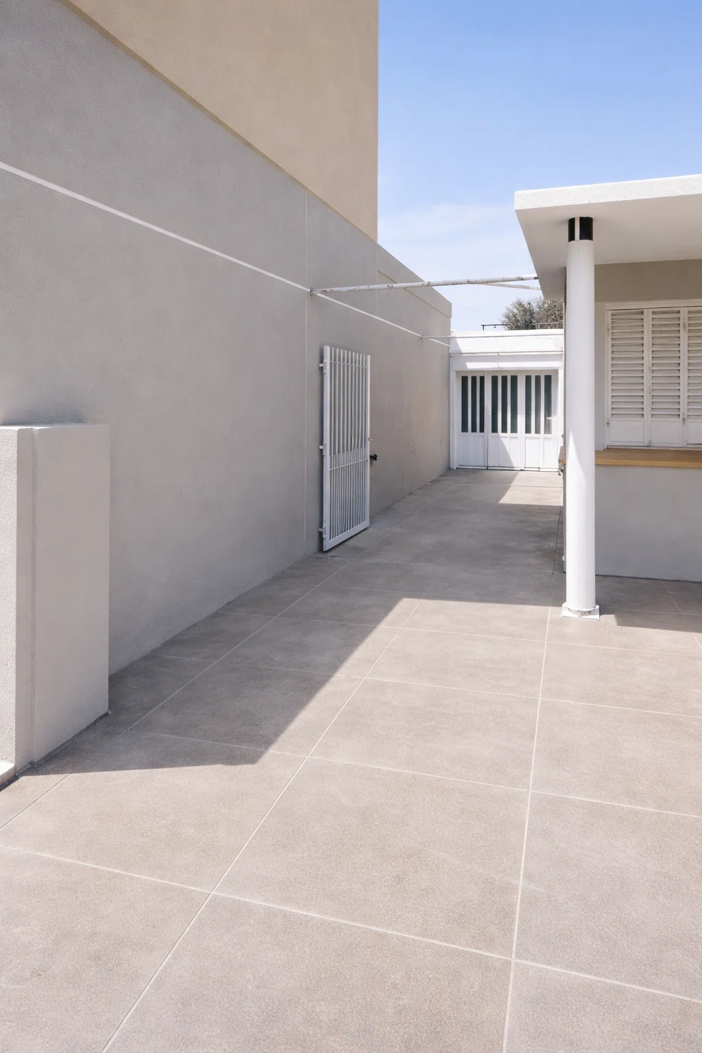 ممر خارجي بجانب المنزل بعد الترميم يظهر أرضيات بلاط حديثة وجدران مطلية بلون رمادي مع بوابة حديد بيضاء