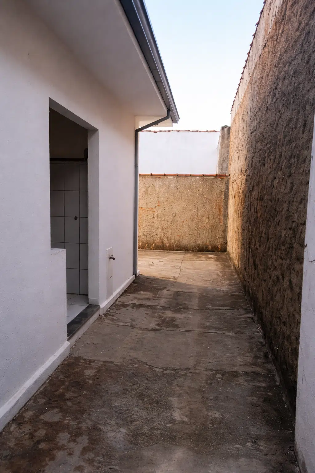 ممر خارجي ضيق بجانب المنزل بأرضية خرسانية قديمة وجدران متآكلة يظهر قبل تنفيذ أعمال الترميم