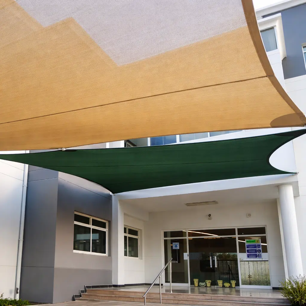 مدخل مبنى حديث بواجهة بيضاء ورمادية تغطيه مظلتان شراعيتان بلون بيج وأخضر مشدودتان فوق الدرج الرخامي