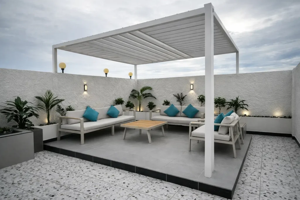 جلسة خارجية في الدمام مع برجولا بيضاء وأرضية بلاط مرتفع وكنب خارجي مزود بوسائد تركواز مع تنسيق نباتات وإضاءة جدارية