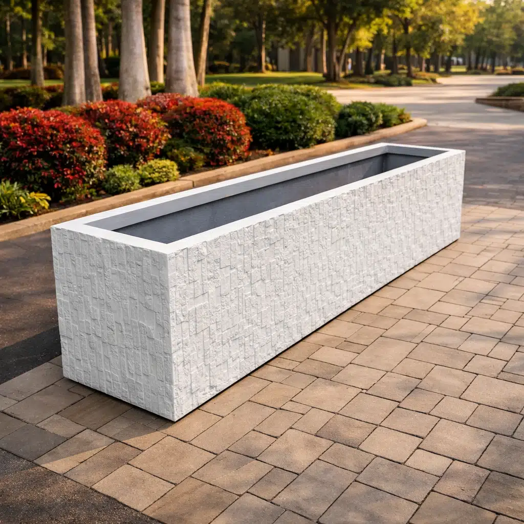 حوض زراعي مستطيل بتشطيب حجري أبيض بارز يوضع فوق أرضية مرصوفة، بتصميم عصري مناسب للممرات والحدائق العامة