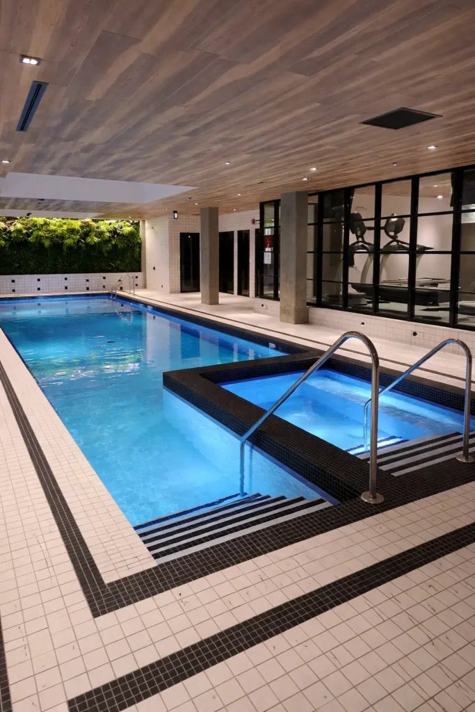 مسبح داخلي فاخر بتصميم عصري يحتوي على جاكوزي مرتفع بإضاءة مائية زرقاء، مع درج نزول آمن وأرضيات سيراميك