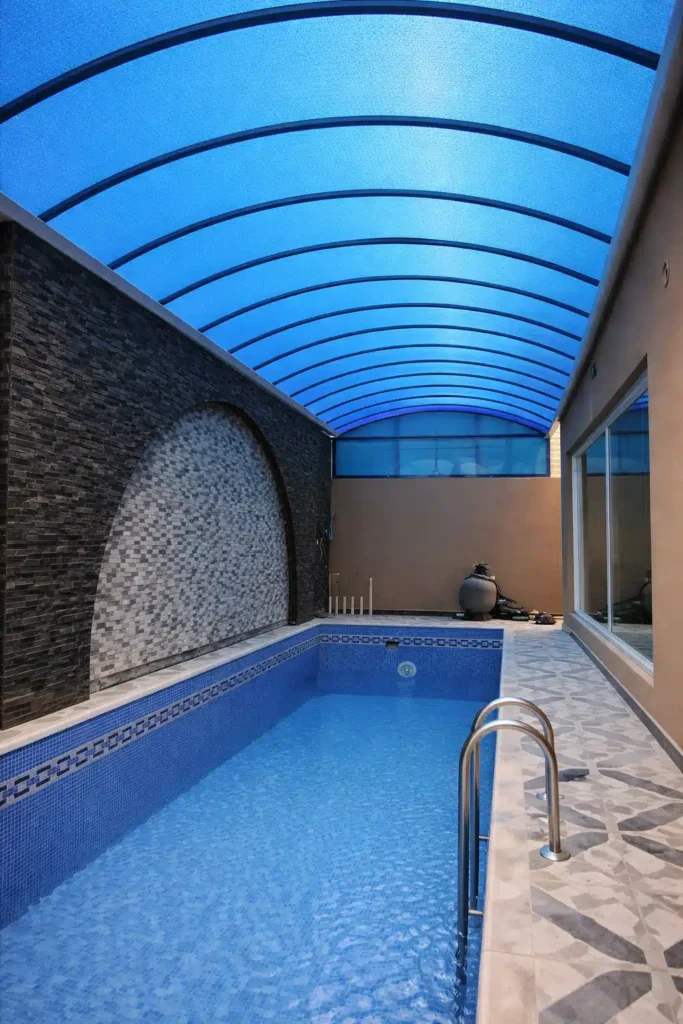 مظلة بولي كربونيت زرقاء مقوسة تغطي مسبح منزلي لتوفير الظل والحماية من أشعة الشمس